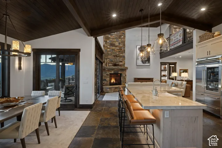 Open-concept living space featuring a vaulted, wood-plank ceiling, floor-to-ceiling stone fireplace, large kitchen island with countertop seating, and stone flooring