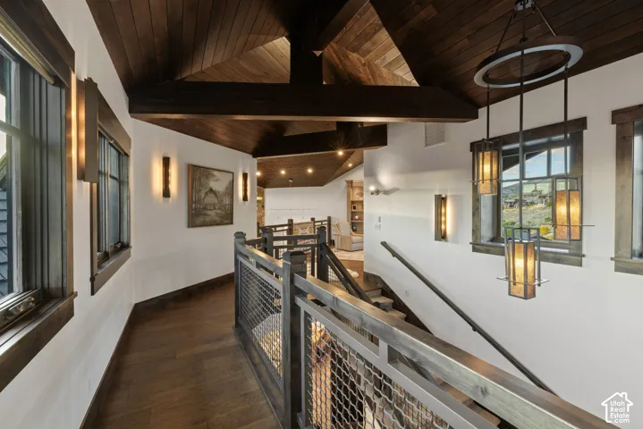 Vaulted wood-plank ceiling featuring exposed structural beams, wood-finish flooring, custom wood window trim, industrial-style metal wire railing, and decorative multi-tiered pendant lighting