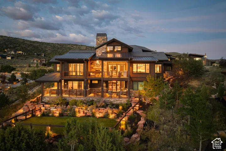 Multi-level exterior featuring wood siding, stone masonry, a standing-seam metal roof, multiple covered decks, and tiered stone retaining walls