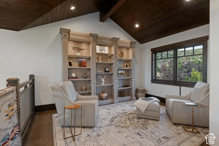 Vaulted wood-plank ceiling featuring exposed structural beams, built-in floor-to-ceiling cabinetry with decorative molding, and metal mesh railing