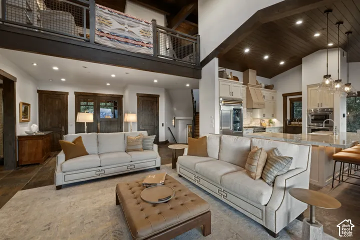 Vaulted ceiling with dark wood-plank finish, open-railing upper mezzanine, built-in cabinetry, recessed lighting, and stone-surface kitchen island