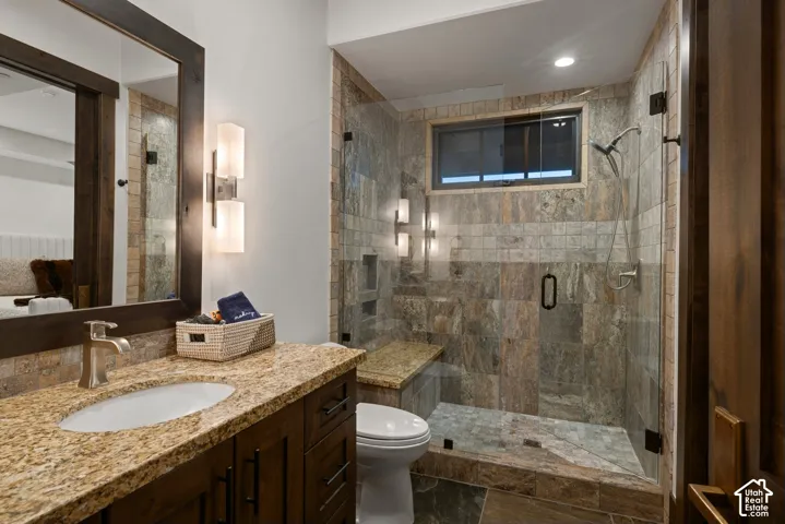 Bathroom featuring dark wood-finish cabinetry, natural stone countertop with an integrated basin, glass-enclosed shower with full-height stone tile surround, built-in shower bench, and dual-sconce vanity lighting
