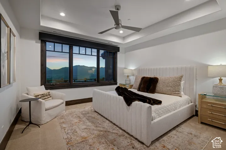Tray ceiling with recessed lighting, multi-pane window with dark wood trim, modern ceiling fan, and carpeted flooring