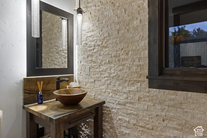 Stacked stone accent wall with a custom wood-surface vanity, round vessel sink, matte black hardware, and dark wood-trimmed mirror and window frame