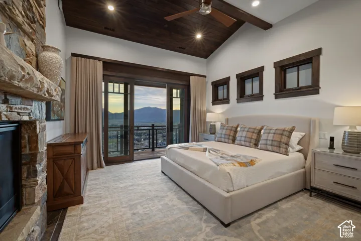 Vaulted ceiling with dark wood-finish planking, stone fireplace, multi-panel glass door leading to a balcony, and dark wood-trimmed casement windows