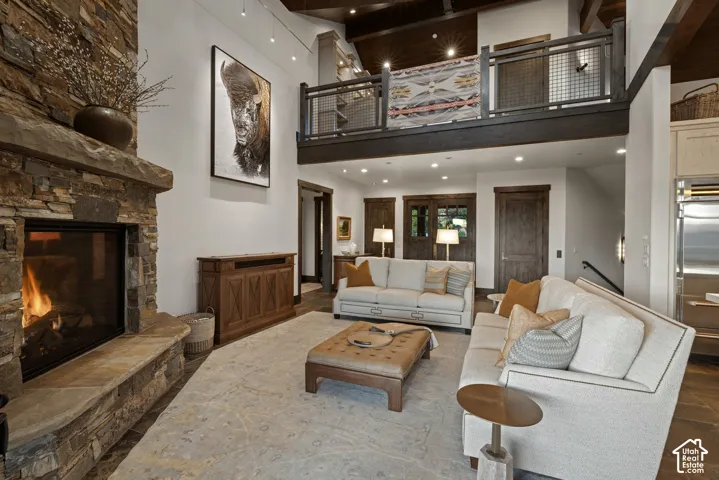 Floor-to-ceiling stone fireplace, vaulted ceiling with exposed timber beams, and a mezzanine level featuring metal railing
