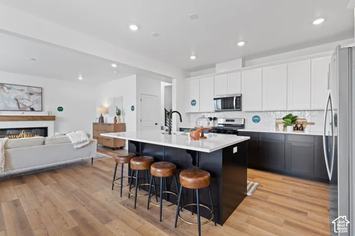Kitchen featuring dual-tone cabinetry, a central island with a solid surface countertop, wood-finish flooring, recessed lighting, and an integrated fireplace