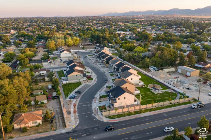 Aerial perspective featuring a residential subdivision with paved roadways, managed green space, integrated walking paths, and mountain backdrops