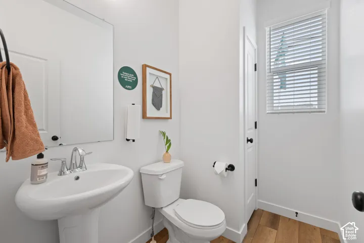 Powder room featuring a pedestal sink, polished chrome faucet, rectangular wall-mounted mirror, wood-finish flooring, and a window with horizontal blinds