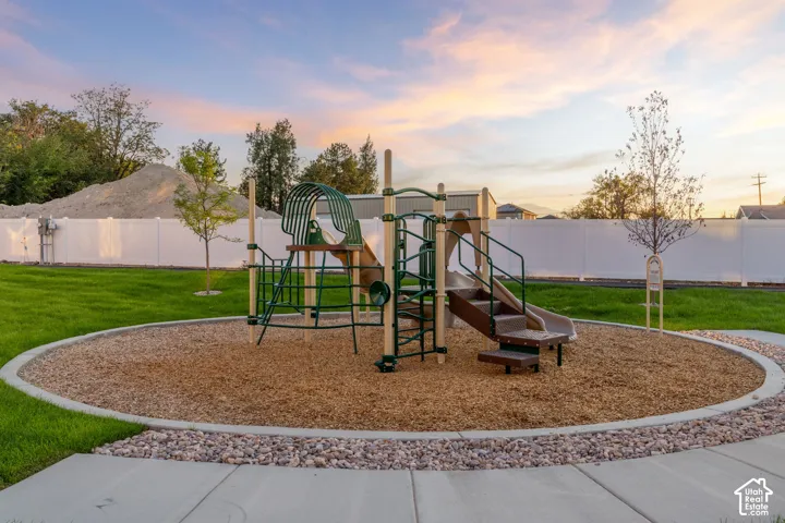 Manicured lawn featuring a circular playground area with built-in equipment, white vinyl fencing, and concrete hardscaping