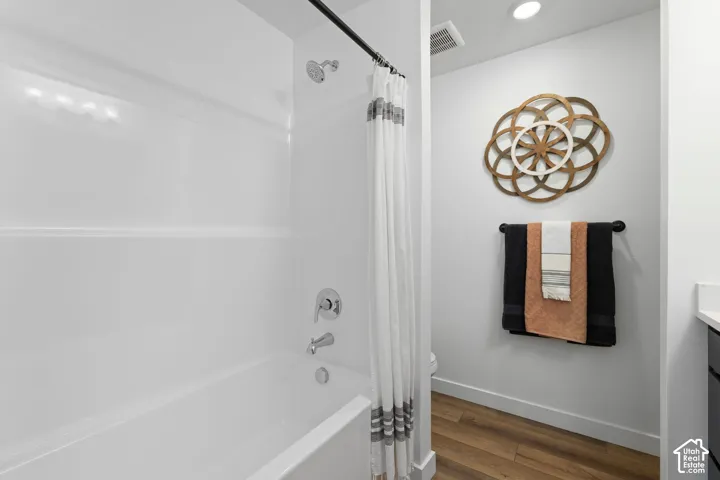 Bathtub and shower combination featuring a polished chrome faucet, recessed ceiling lighting, and wood-finish flooring