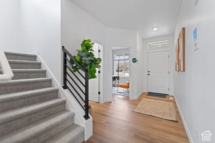 Entryway featuring wood-finish flooring, a staircase with carpeted treads, and a matte black metal horizontal-bar railing
