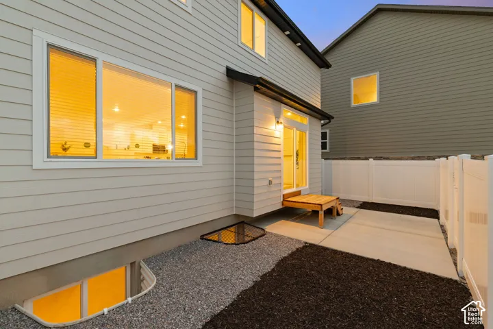 Exterior siding with a concrete patio, wood-finish rear step, white vinyl privacy fencing, and egress window wells