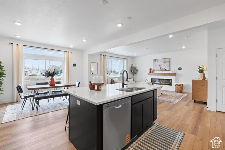Kitchen featuring a center island with light-toned countertops and dark cabinetry, wood-finish flooring, recessed lighting, and a linear fireplace with a natural wood mantel