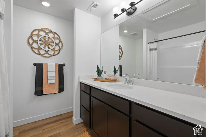 Bathroom vanity featuring dark-finished cabinetry, a white countertop with an integrated sink, a large wall-mounted mirror, modern multi-bulb lighting, and wood-finish flooring