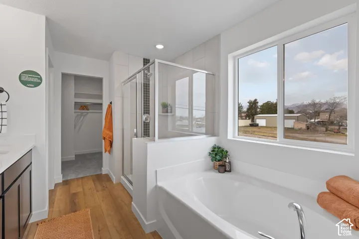 Bathroom featuring an oval soaking tub, a glass-enclosed shower with tiled surround, wood-finish flooring, dark-toned cabinetry, and large window with mountain scenery