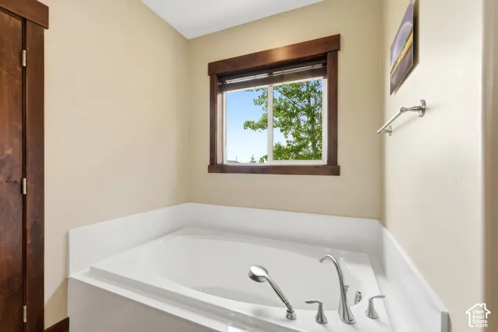 Oval drop-in soaking tub featuring a deck-mounted hand shower and polished metal fixtures, framed by wood trim molding and a window with wood casing
