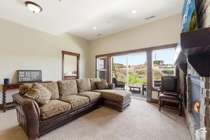 Living area featuring vaulted ceilings, floor-to-ceiling stone fireplace, stained wood trim, and large sliding glass door with external patio access