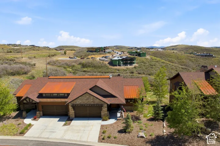 Mountain-inspired exterior featuring stone masonry, metal roofing accents, shingle roof, two-car garage, and desert landscape