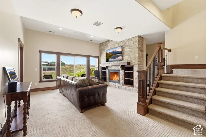 Living area featuring floor-to-ceiling stone fireplace, custom built-in shelving, wooden mantel, expansive windows with exterior mountain scenery, and a wooden staircase with decorative metal balusters