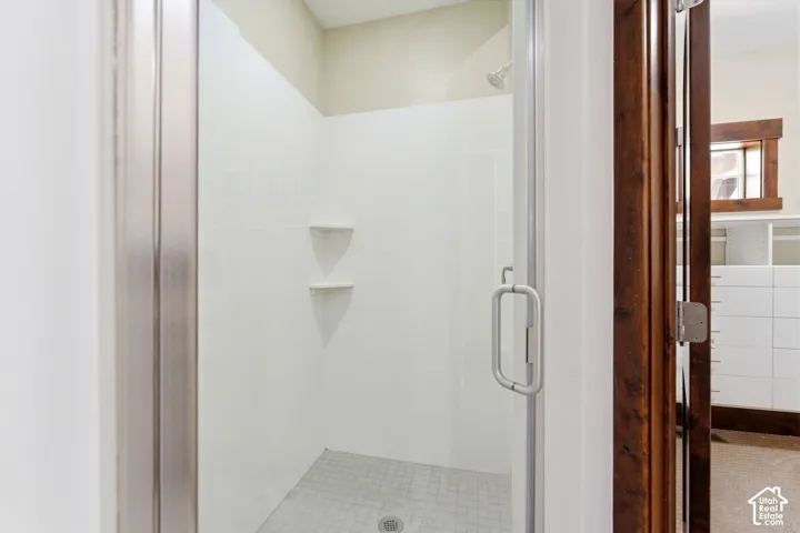 Shower enclosure featuring a glass door, smooth surround panels, built-in corner shelving, and a tiled floor