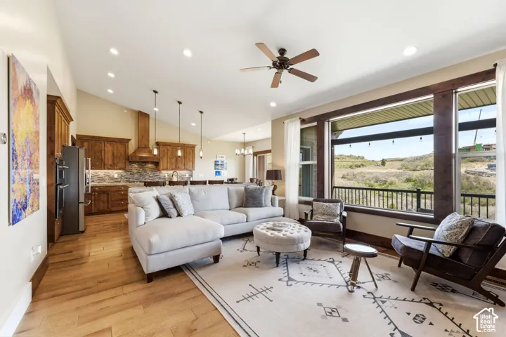 Open-concept living space featuring wood-finish flooring, vaulted ceilings, stained wood cabinetry, stone tile backsplash, and oversized windows