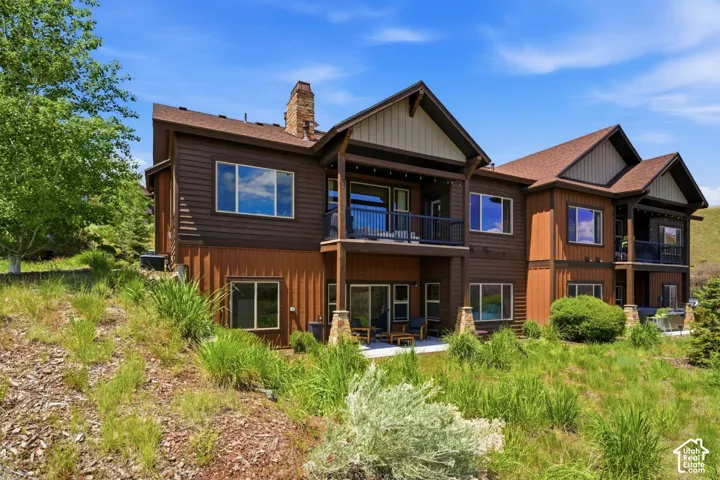 Multi-level exterior featuring wood siding, stone chimney masonry, covered balconies with metal railings, and a concrete patio