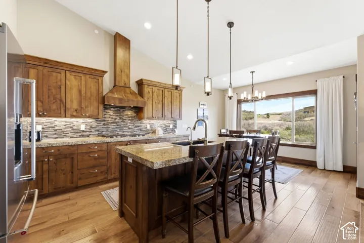 Kitchen featuring custom wood cabinetry, a stone-tiled backsplash, a large center island with a stone countertop, recessed lighting, and wood-finish flooring