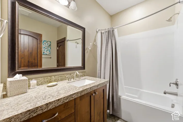Bathroom featuring a wood vanity with a stone countertop, an integrated sink, a framed wall mirror, and a tub-shower combination with brushed metal fixtures