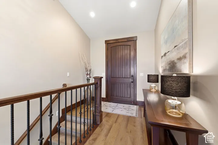 Entryway featuring a solid wood door with vertical plank detailing, wood-finish flooring, and a staircase with stained wood handrails and black metal balusters