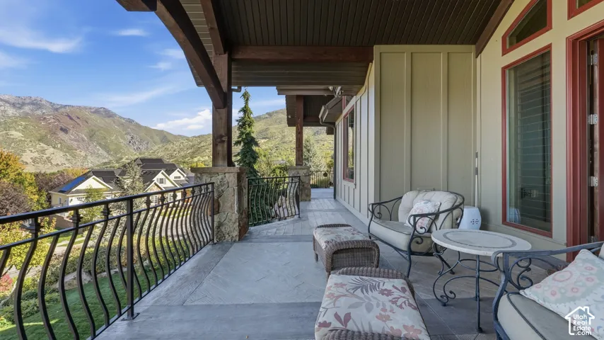 Covered deck featuring wood-beam construction, natural stone pillars, decorative iron railing, and patterned paver flooring with a mountain backdrop