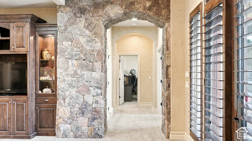 Custom stone-clad arched entry, floor-to-ceiling wood cabinetry with glass display panels, and plantation shutters