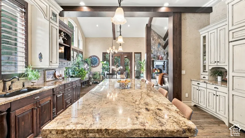 Kitchen featuring a spacious stone-topped island, custom two-tone cabinetry, recessed and pendant lighting, wood-finish flooring, and exposed timber beams