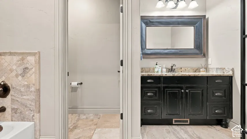 Black vanity with multi-drawer storage, stone countertop, framed wall mirror, stone-tile flooring, and decorative wall tiling