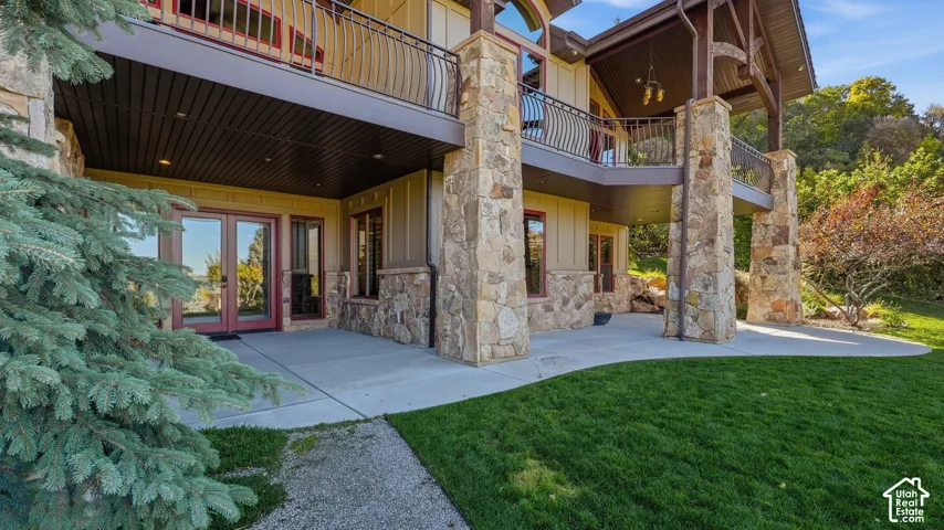 Multi-level exterior featuring stacked stone columns, concrete patio, upper-level metal railing balconies, and wood-paneled soffits