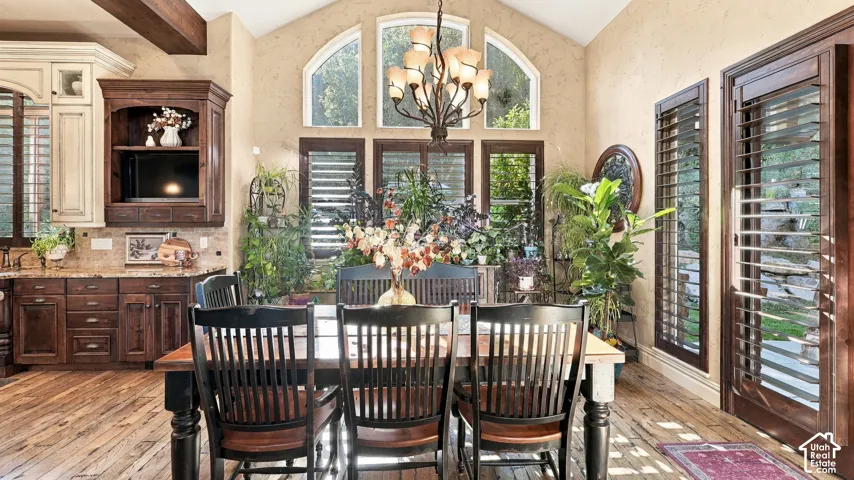 Vaulted ceiling featuring exposed timber beams, custom wood cabinetry, multi-paned arched windows, decorative iron chandelier, and wood-finish flooring