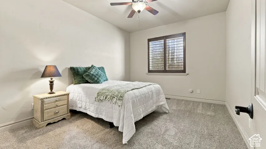 Neutral-toned bedroom featuring carpeting, an integrated ceiling fan with light fixture, and a window equipped with dark wood plantation shutters