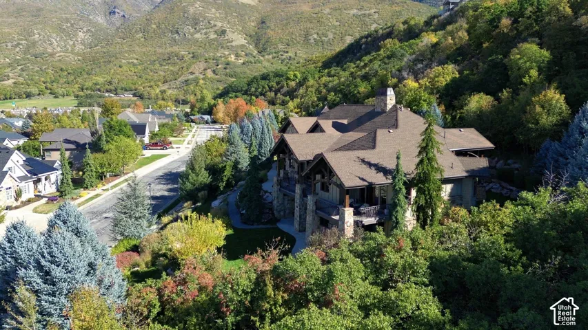 Multi-level estate featuring stone and timber exterior detailing, multi-pitched roofline, stone chimney, and covered outdoor deck space set against a mountainous backdrop