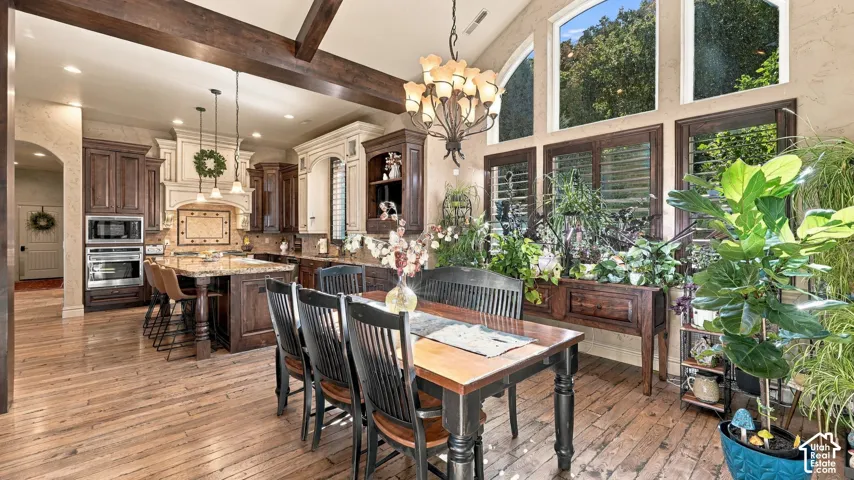Vaulted ceiling featuring exposed wood beams, oversized arched windows, wood-finish flooring, custom wood cabinetry, and a stone-topped kitchen island