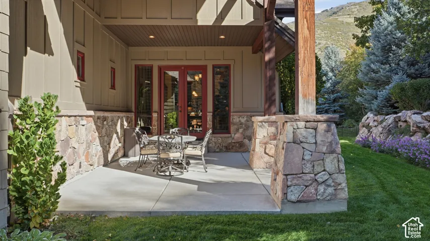 Covered patio featuring stone masonry wainscoting, timber support posts, concrete flooring, and double-door entry