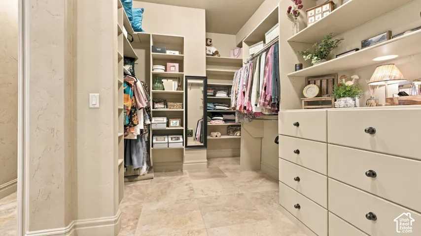 Custom walk-in closet featuring extensive built-in shelving, a wall-mounted mirror, stone-finish tile flooring, and integrated dresser cabinetry with matte hardware