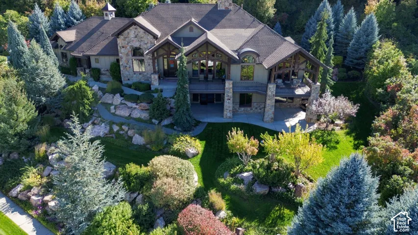 Multi-level mountain-style residence featuring stone masonry cladding, timber-frame accents, expansive elevated deck, covered patio, and landscaped grounds with stone terracing