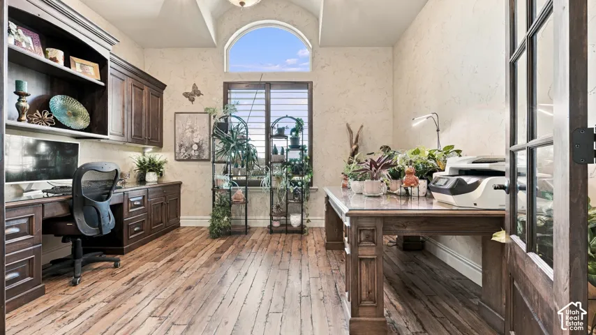 Wood-finish flooring, vaulted ceiling, arched transom window, built-in dark wood cabinetry, and French doors