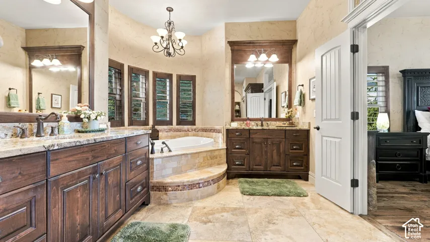 Bathroom featuring dual dark-wood vanities with stone countertops, tiled soaking tub platform, stone floor tile, and crown-molding cabinetry