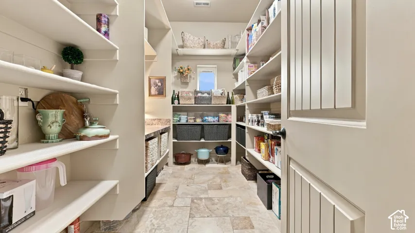 Walk-in pantry featuring stone-tile flooring, multi-level built-in shelving, stone-finish countertops, and an operable window