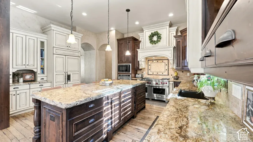 Kitchen featuring a central island with stone countertops, custom cabinetry in contrasting finishes, wood-finish flooring, a decorative range hood, and stainless-steel appliances