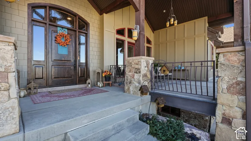 Covered entryway featuring a solid wood door with arched glass surround, decorative stone masonry, board-and-batten siding, and wrought-iron railing