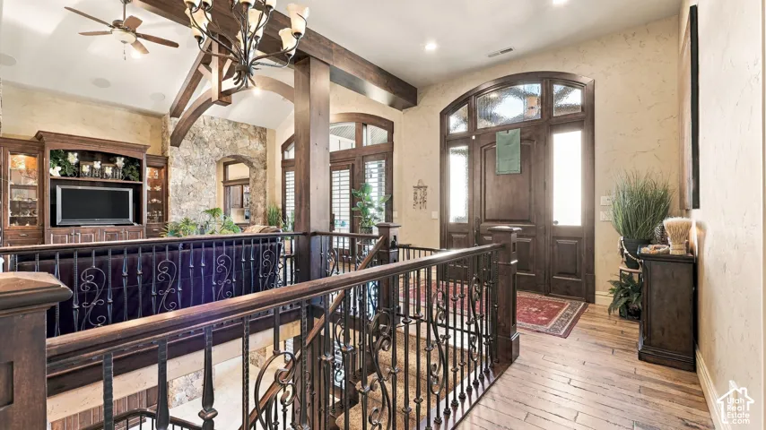 Vaulted ceilings with exposed timber trusses, wrought iron stair railings, custom built-in cabinetry, wood-finish flooring, and arched double-entry doors with transom windows