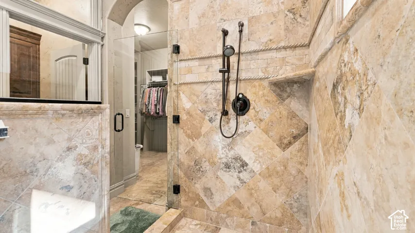 Walk-in shower featuring floor-to-ceiling natural stone tile in a diagonal pattern, stone-finish corner shelving, a glass door with matte black hardware, and an adjustable matte black shower head