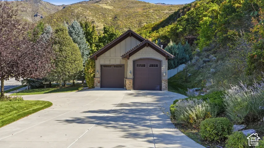 Detached three-car garage featuring board-and-batten siding, stone masonry accents, dual-paneled garage doors, and a concrete driveway